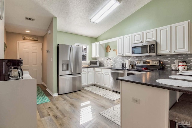 kitchen with kitchen peninsula, appliances with stainless steel finishes, backsplash, and white cabinetry