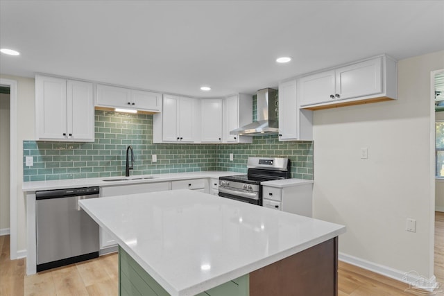 kitchen featuring sink, wall chimney range hood, appliances with stainless steel finishes, white cabinets, and light wood-type flooring