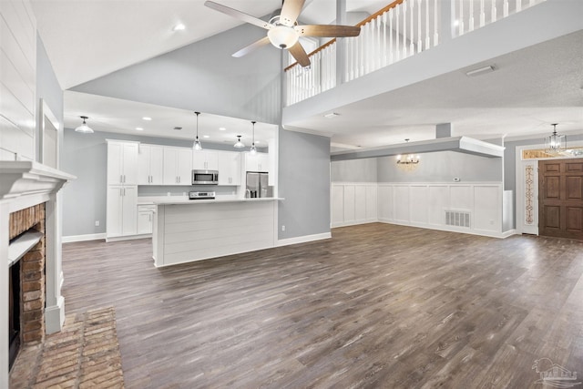 unfurnished living room featuring a brick fireplace, ceiling fan with notable chandelier, a textured ceiling, dark wood-type flooring, and high vaulted ceiling