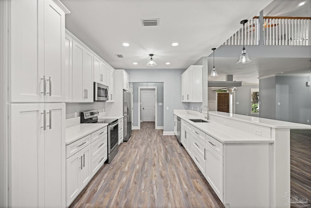 kitchen featuring sink, hanging light fixtures, kitchen peninsula, white cabinets, and appliances with stainless steel finishes