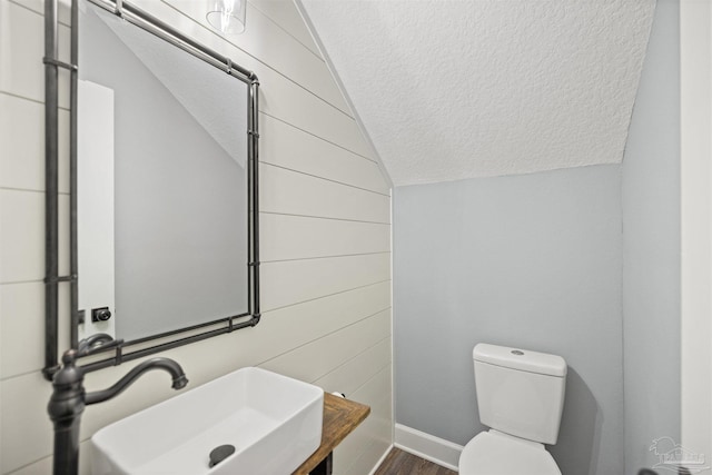 bathroom featuring lofted ceiling, sink, hardwood / wood-style flooring, toilet, and a textured ceiling