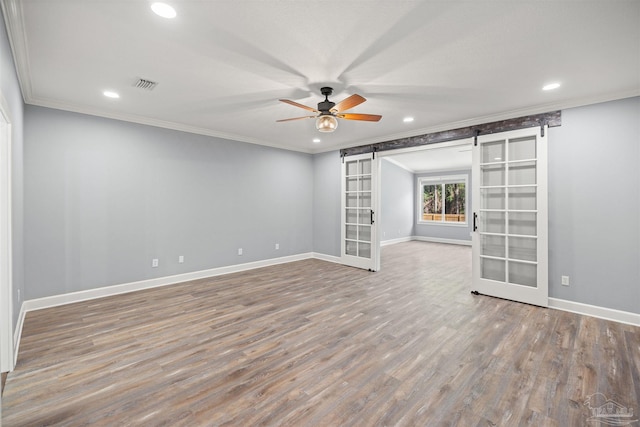 spare room featuring hardwood / wood-style floors, french doors, crown molding, ceiling fan, and a barn door