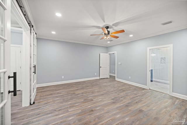 spare room with a barn door, ceiling fan, wood-type flooring, and ornamental molding