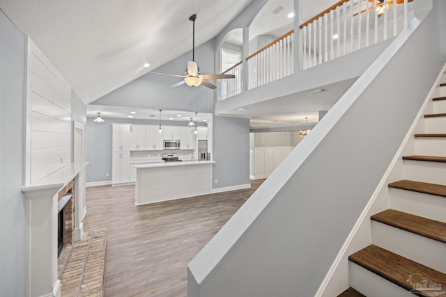 staircase featuring hardwood / wood-style floors, ceiling fan, high vaulted ceiling, and a brick fireplace