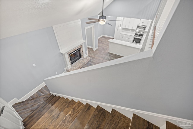 stairs featuring wood-type flooring, vaulted ceiling, ceiling fan, and a brick fireplace