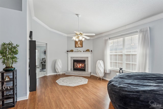 bedroom featuring a textured ceiling, hardwood / wood-style flooring, ceiling fan, a tile fireplace, and crown molding