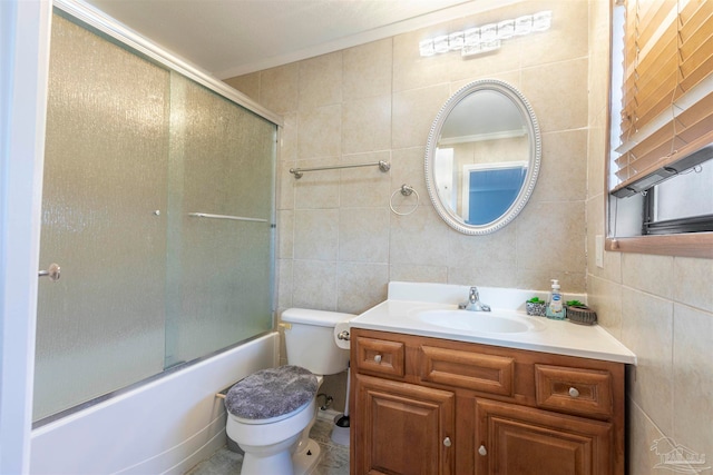 full bathroom featuring bath / shower combo with glass door, vanity, toilet, and tile walls