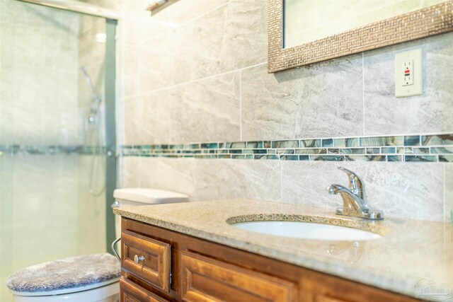 bathroom with tile walls, a shower with door, backsplash, vanity, and toilet