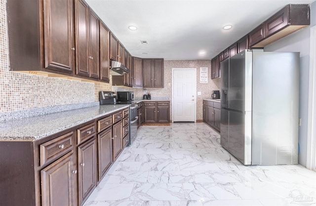 kitchen with dark brown cabinetry, appliances with stainless steel finishes, backsplash, and light stone countertops