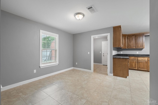 kitchen with brown cabinets, dark countertops, baseboards, light tile patterned floors, and visible vents