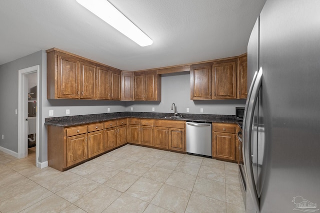 kitchen featuring dark stone counters, brown cabinets, a sink, light tile patterned floors, and stainless steel appliances