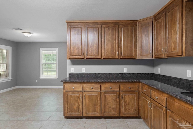 kitchen featuring dark stone counters, baseboards, and brown cabinets