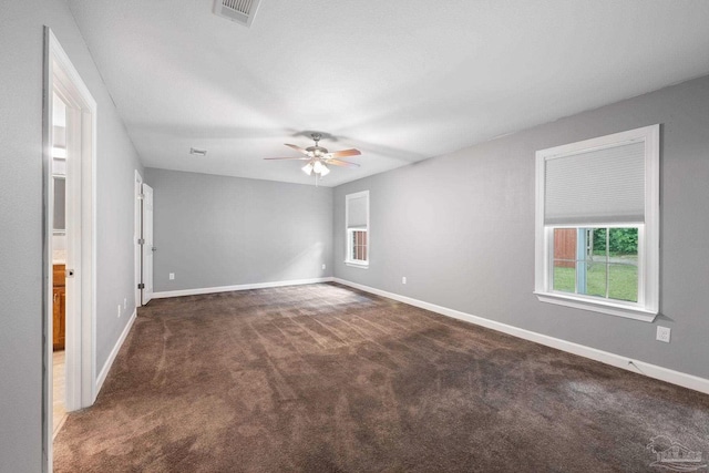 unfurnished room featuring visible vents, baseboards, dark carpet, and ceiling fan