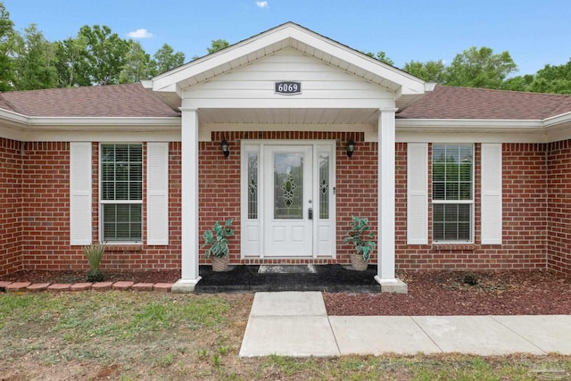 view of exterior entry with a shingled roof and brick siding