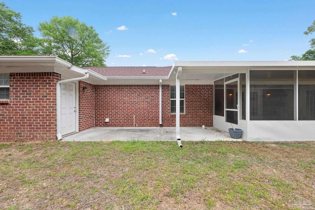 back of property with a sunroom, a yard, a patio area, and brick siding