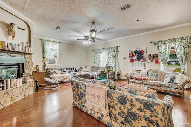 living room with a stone fireplace, wood-type flooring, ornamental molding, ceiling fan, and a textured ceiling