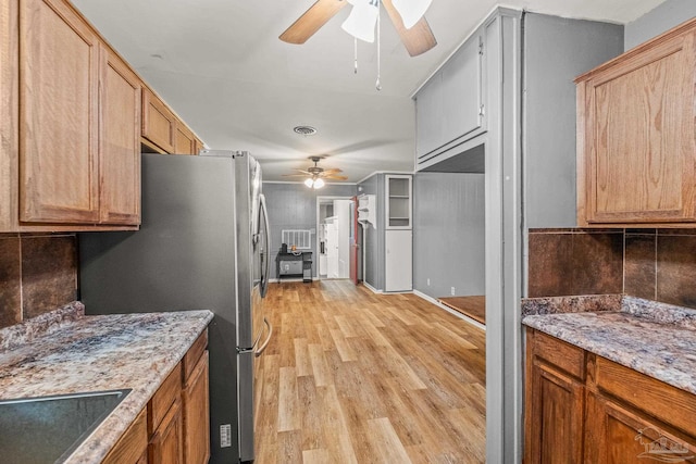 kitchen with ceiling fan, tasteful backsplash, light stone counters, light hardwood / wood-style flooring, and stainless steel fridge