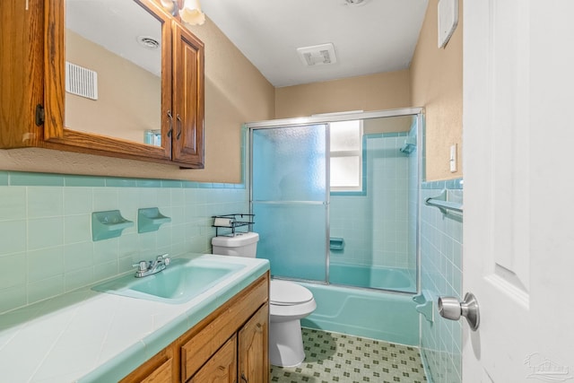 full bathroom featuring vanity, toilet, tile walls, and bath / shower combo with glass door