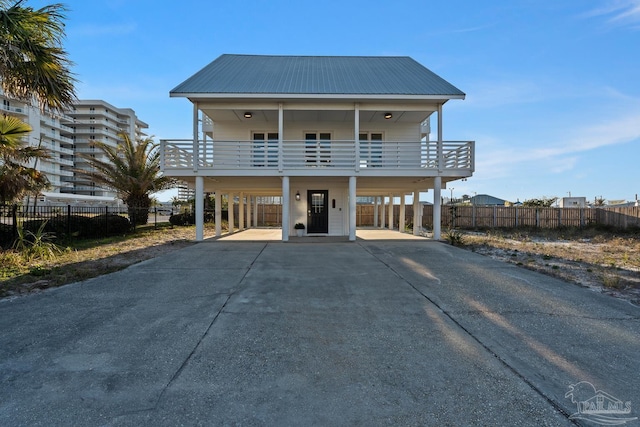 coastal inspired home with metal roof, driveway, a carport, and fence