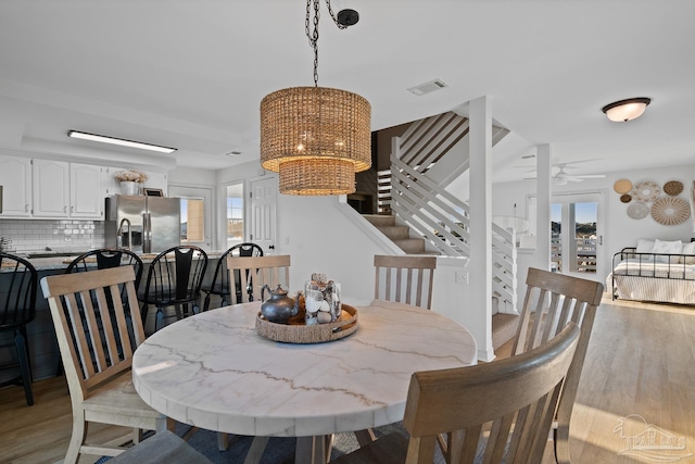 dining area featuring light wood-style floors, visible vents, ceiling fan, and stairs