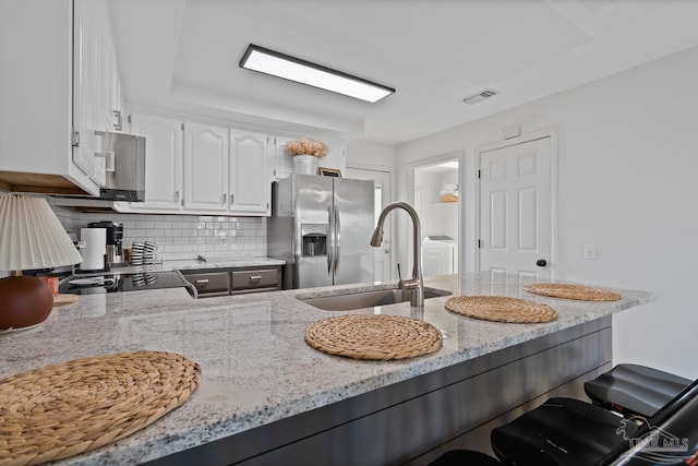 kitchen with light stone counters, a sink, white cabinets, stainless steel refrigerator with ice dispenser, and decorative backsplash