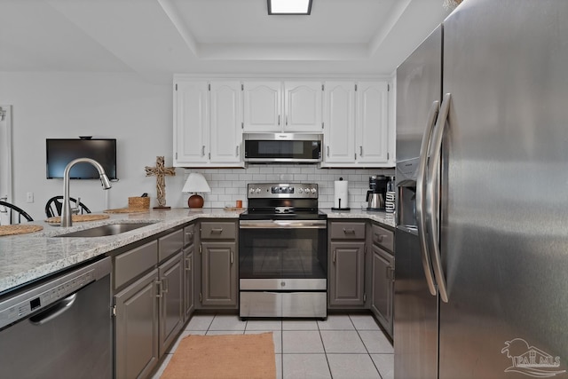 kitchen with stainless steel appliances, a tray ceiling, gray cabinets, and a sink