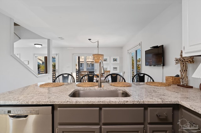 kitchen featuring dishwasher, a sink, a wealth of natural light, and light stone countertops