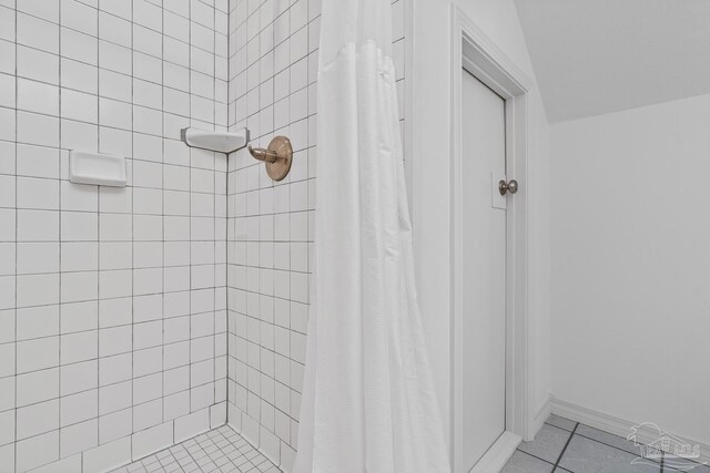 bathroom with tile patterned flooring, a tile shower, and baseboards
