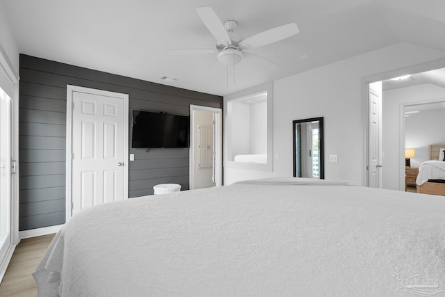 bedroom with light wood finished floors, vaulted ceiling, a ceiling fan, and wood walls
