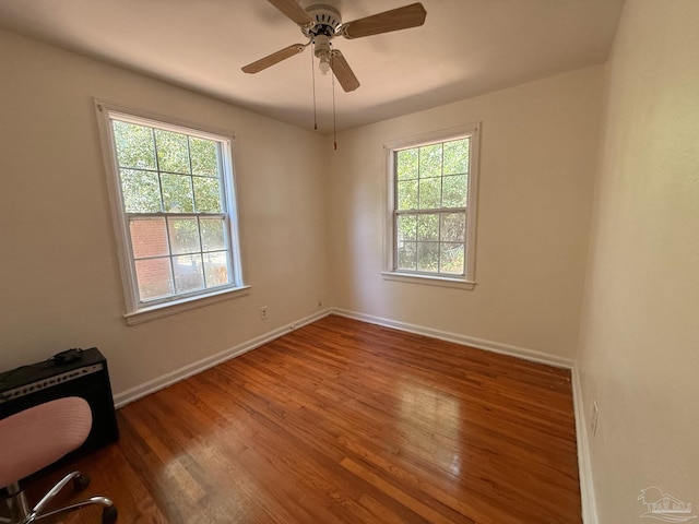 spare room featuring baseboards, ceiling fan, wood finished floors, and a healthy amount of sunlight