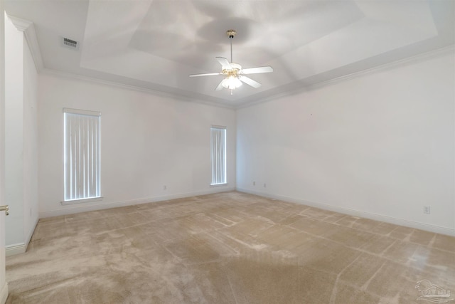 spare room with a ceiling fan, a raised ceiling, light colored carpet, ornamental molding, and visible vents