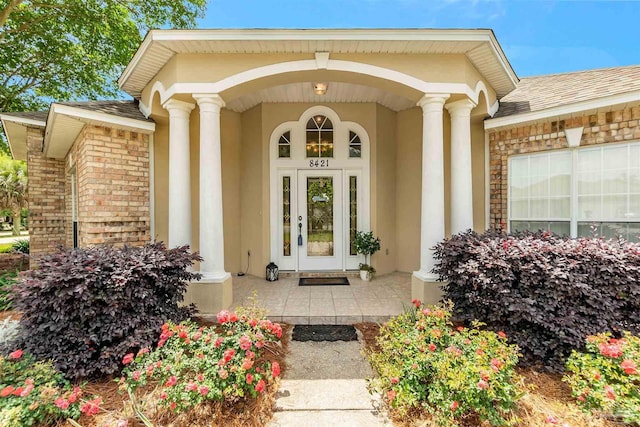 entrance to property featuring stucco siding, a shingled roof, and covered porch