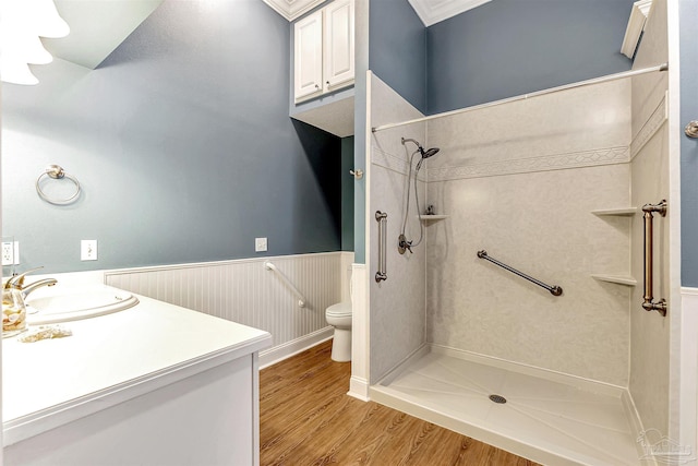 bathroom with wood finished floors, toilet, tiled shower, and wainscoting