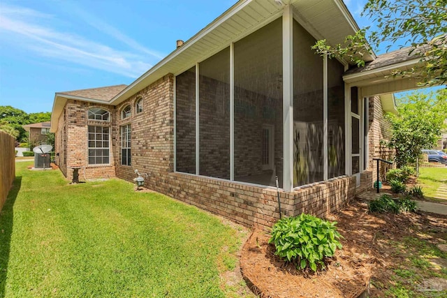 back of house with brick siding, a yard, a sunroom, and roof with shingles