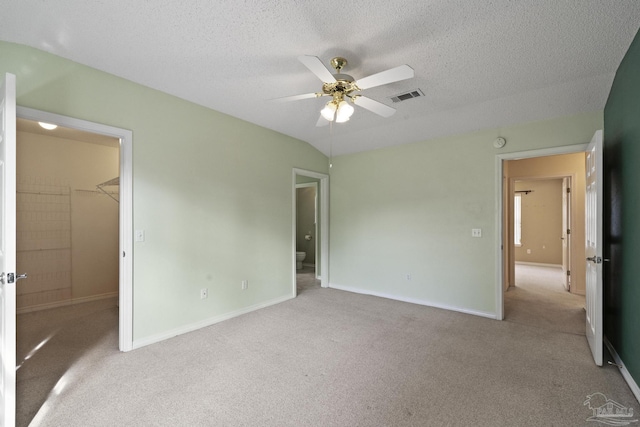 unfurnished bedroom featuring a textured ceiling, a spacious closet, light carpet, ceiling fan, and a closet