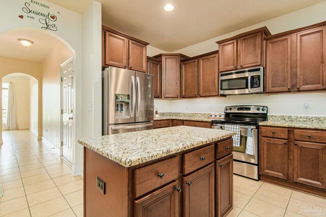 kitchen featuring light tile patterned flooring, a center island, light stone counters, appliances with stainless steel finishes, and a textured ceiling