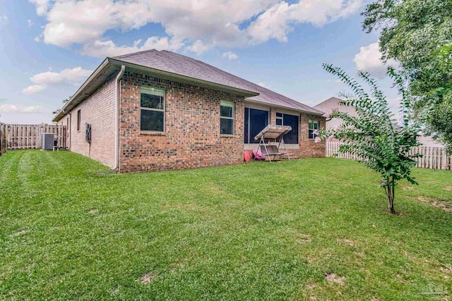 rear view of property featuring central air condition unit and a lawn