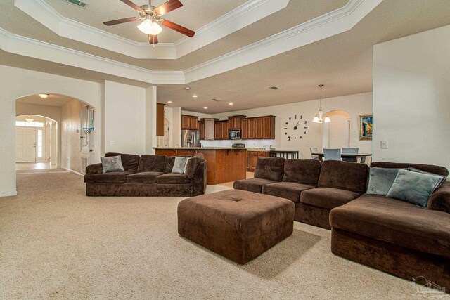 living room featuring ceiling fan, light carpet, crown molding, and a tray ceiling