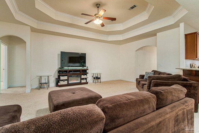 carpeted living room featuring ceiling fan, a raised ceiling, and ornamental molding