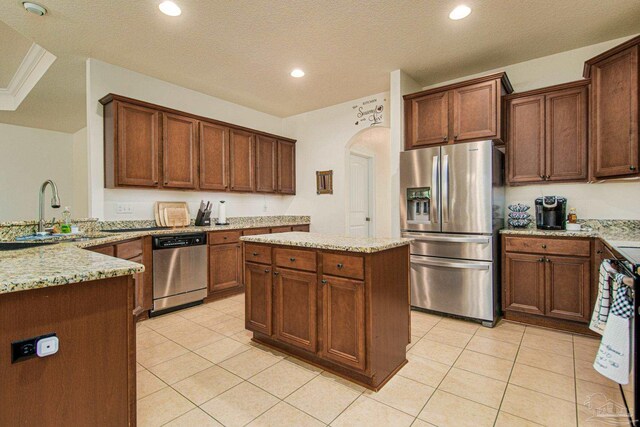 kitchen with appliances with stainless steel finishes, sink, light tile patterned floors, a textured ceiling, and a center island