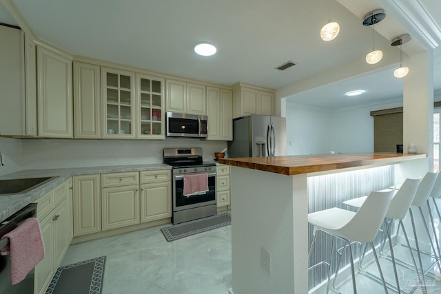 kitchen featuring appliances with stainless steel finishes, wood counters, decorative light fixtures, a kitchen breakfast bar, and cream cabinets