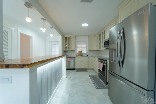 kitchen with wooden counters, appliances with stainless steel finishes, hanging light fixtures, tasteful backsplash, and cream cabinets