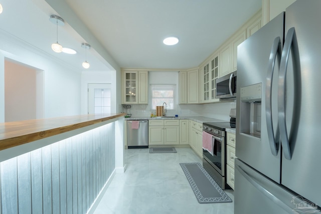 kitchen with sink, hanging light fixtures, stainless steel appliances, tasteful backsplash, and cream cabinets