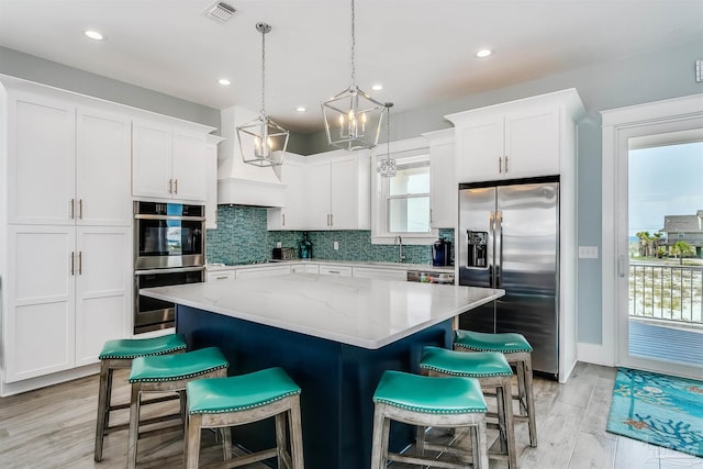 kitchen featuring stainless steel appliances, a kitchen island, visible vents, white cabinetry, and backsplash