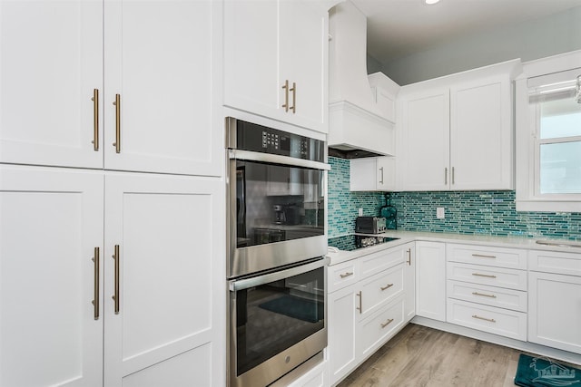 kitchen featuring black electric stovetop, light countertops, custom range hood, backsplash, and double oven