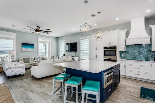 kitchen with oven, visible vents, white cabinets, blue cabinetry, and custom range hood