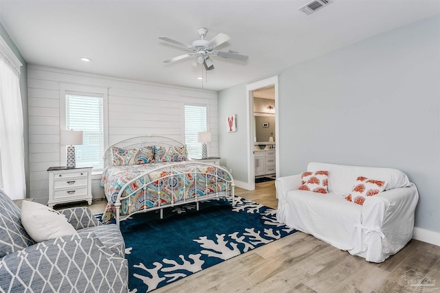 bedroom with baseboards, wood finished floors, visible vents, and connected bathroom