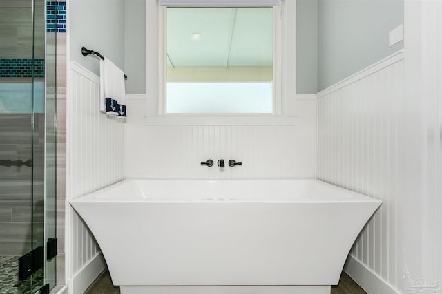 full bath with a wainscoted wall, a stall shower, and a soaking tub