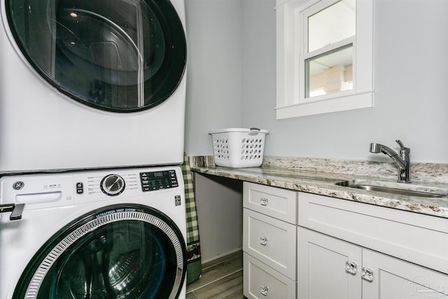 washroom featuring wood finished floors, a sink, cabinet space, and stacked washer / drying machine