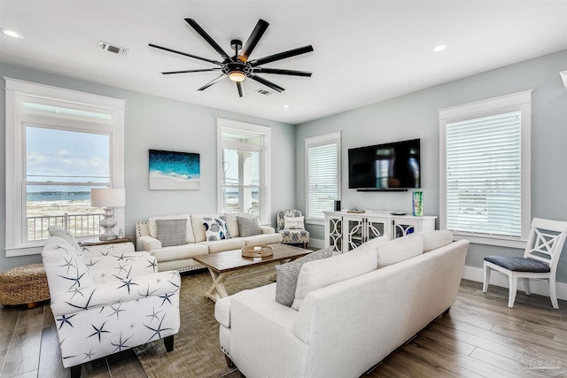 living area with baseboards, wood-type flooring, visible vents, and a ceiling fan